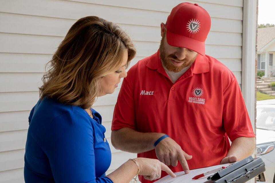 A man and woman in red and blue shirts review a paper related to pest control services in O’Fallon.